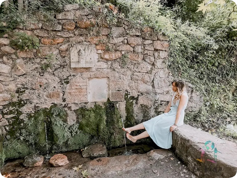 Foto de Judit con un vestido blanco con los pies descalzos en la Fuente de la era Mura