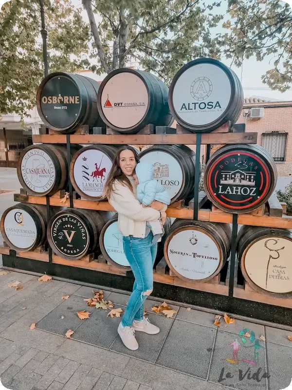 Judit con Eric en brazos delante de barriles con las bodegas de vino de Tomelloso